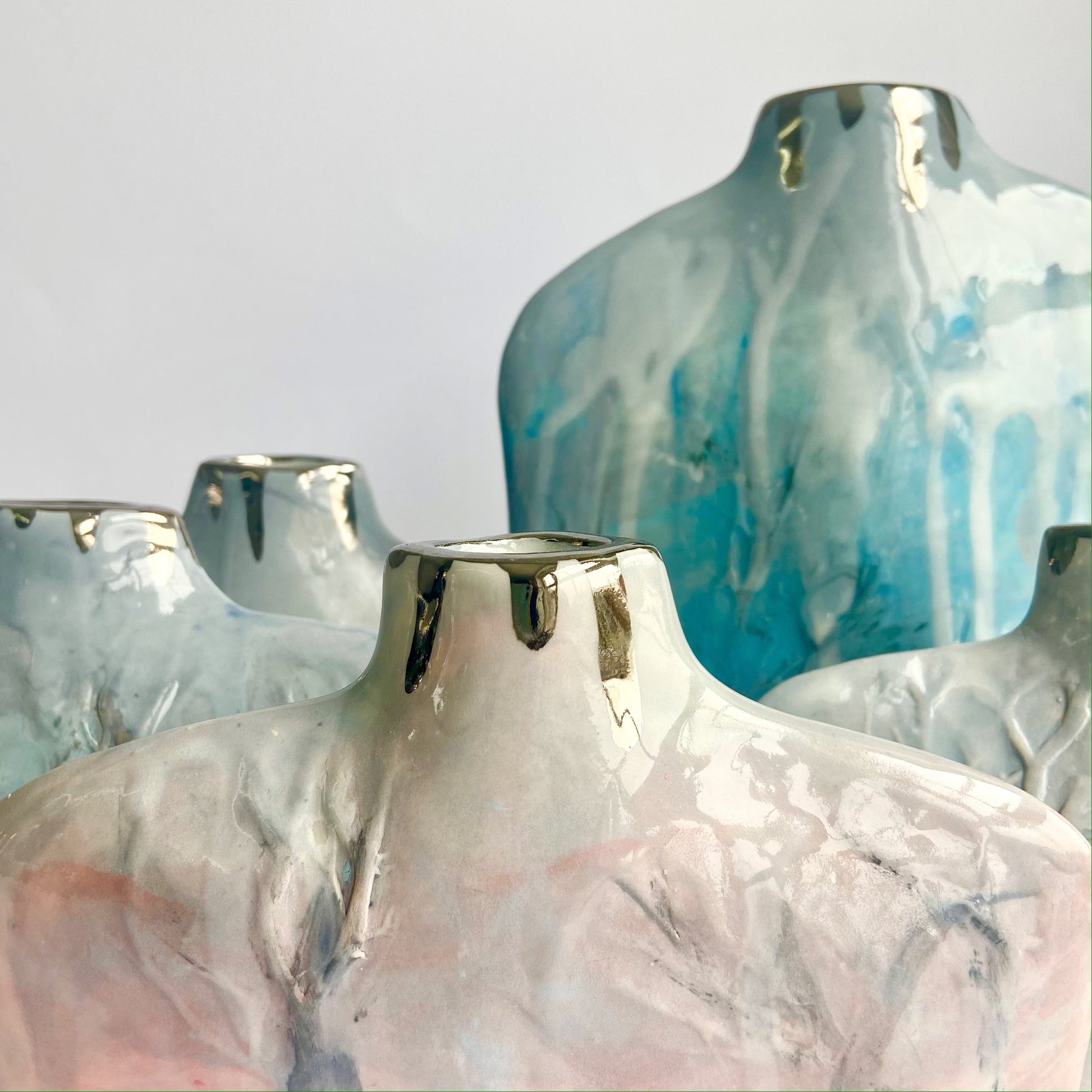 Close up of 5 Silhouette Bottle vases handbuilt in porcelain with relief Winter Tree design in blues, pinks, and greys
