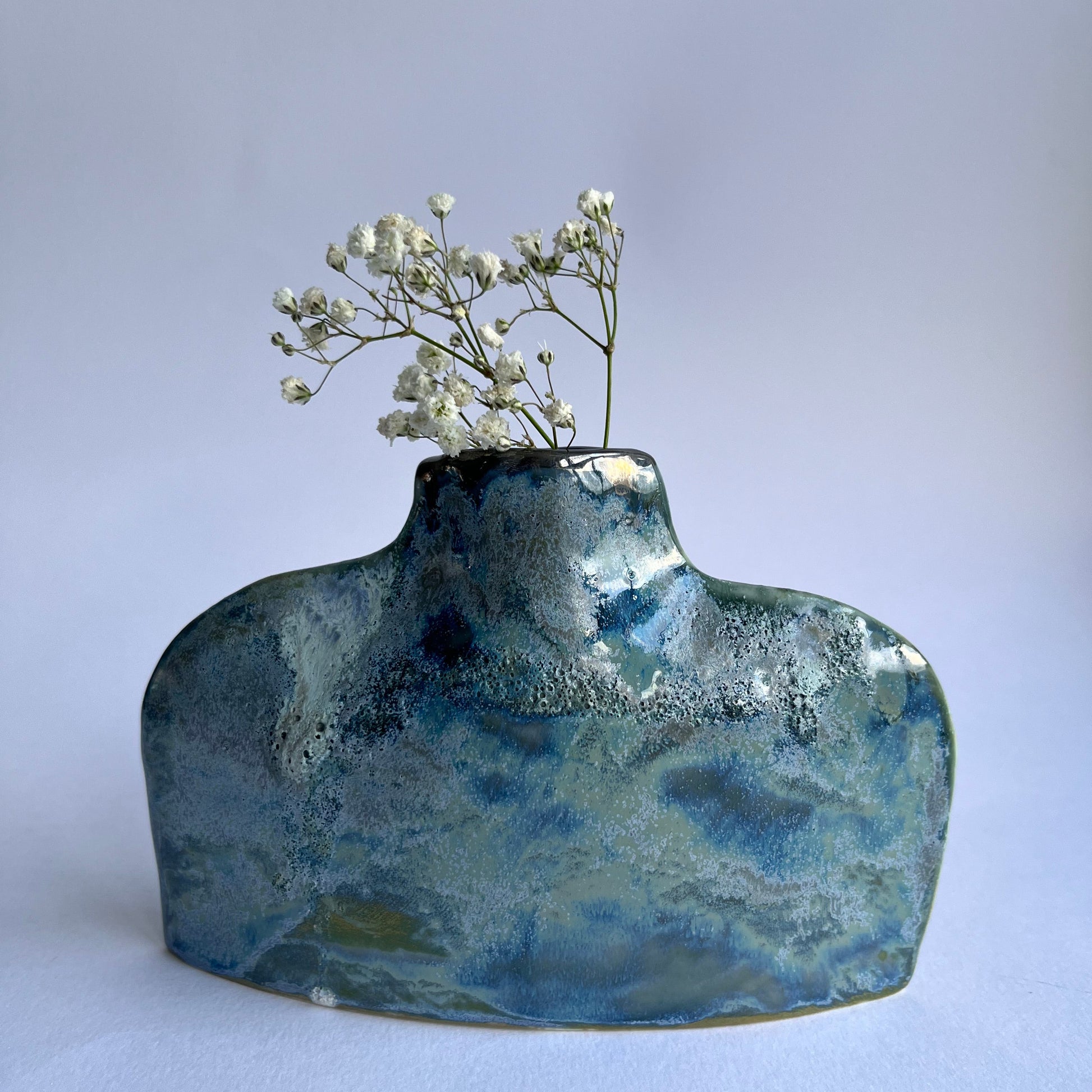 Blue ceramic vase with a textured surface holding small white flowers on a light gray background