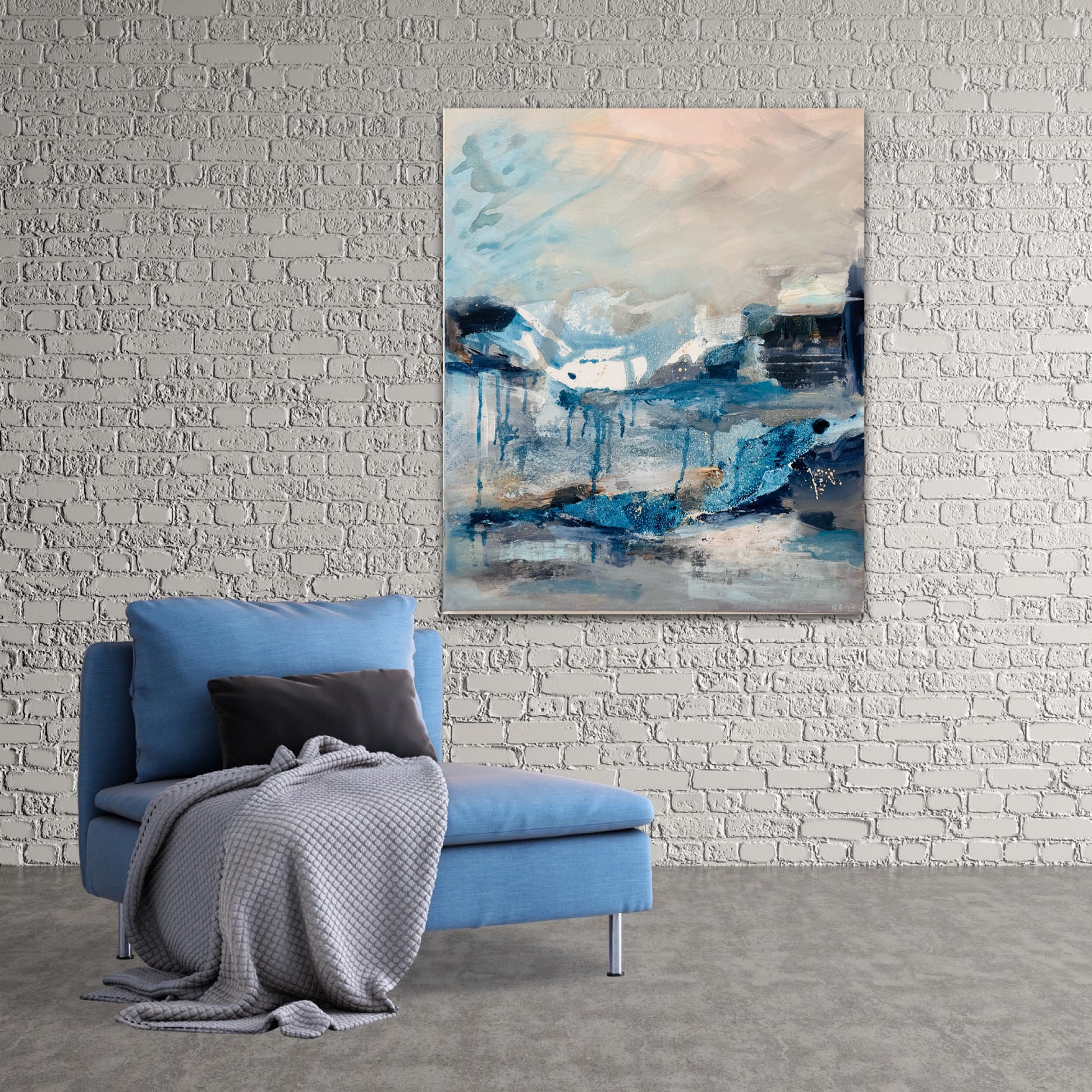 In the Still Air atmospheric landscape artwork with drips and washes of blues grey and peach hung on a grey brick wall with blue chair in front by Nicola Briggs