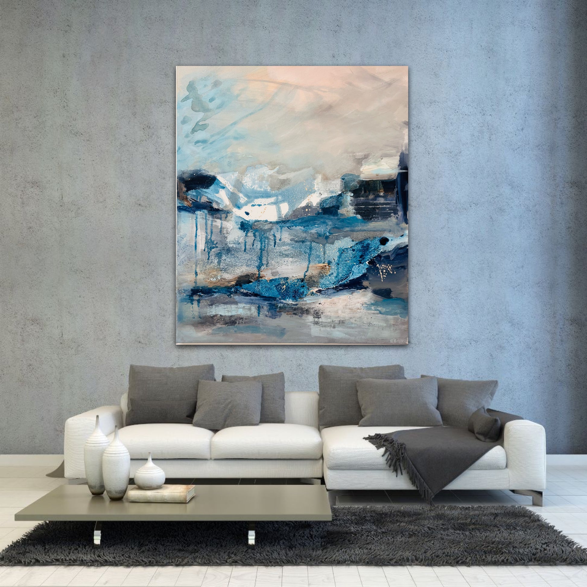 Dramatic expressive artwork painted in blues, greys and peach by artist Nicola Briggs on a grey wall with white modern couch and grey cushions