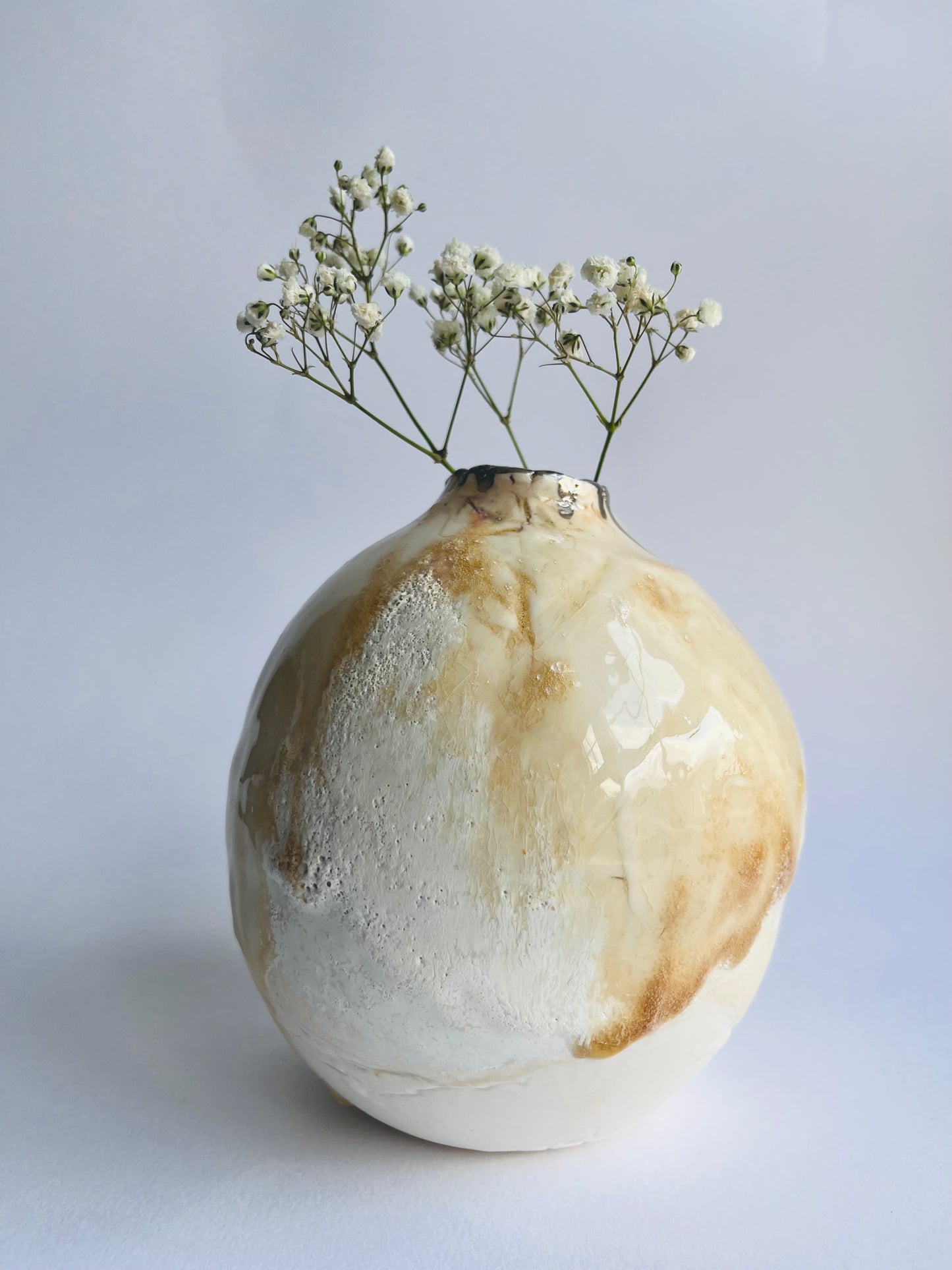 Decorative organic shaped oval vase with a neutral glazes holding small white flowers on a light background