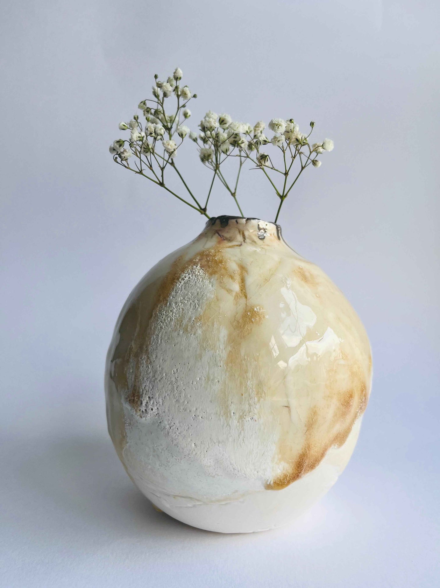 Decorative organic shaped oval vase with a neutral glazes holding small white flowers on a light background