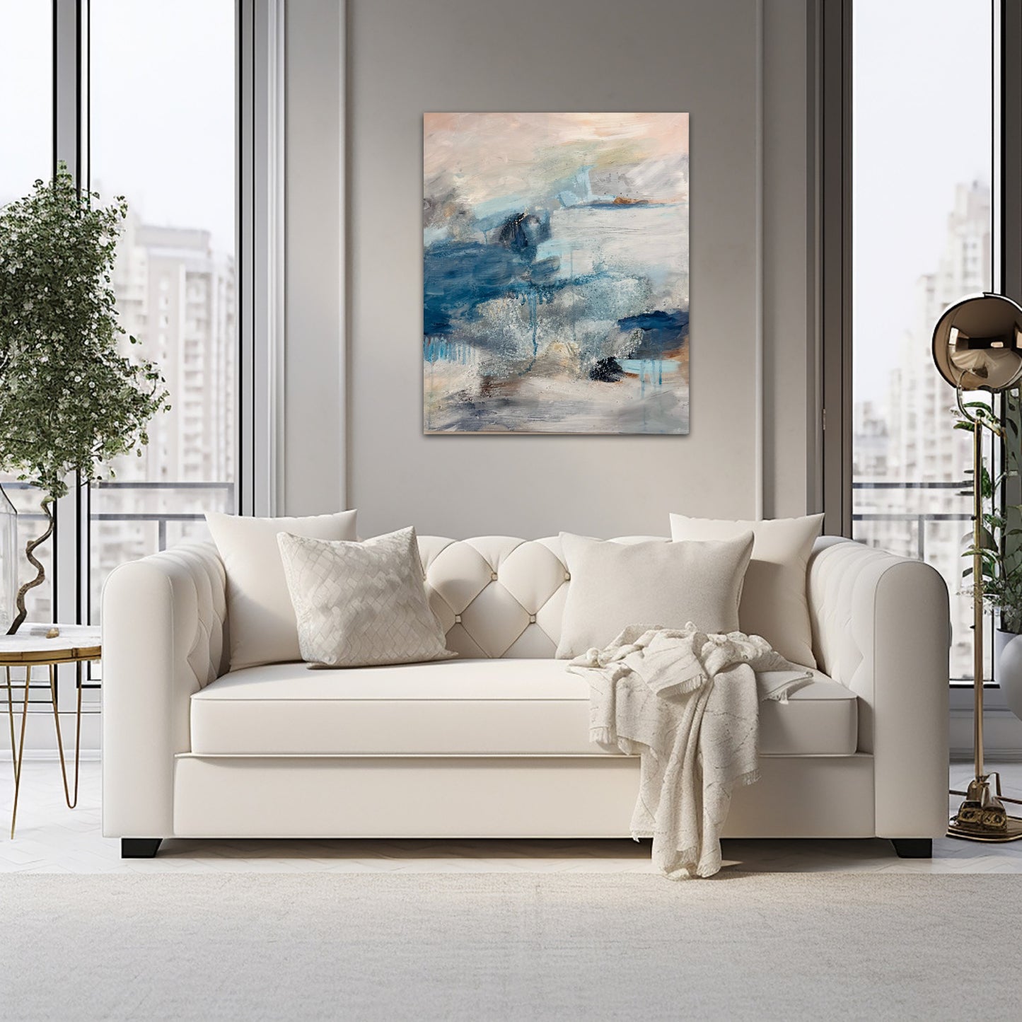 A lifestyle photo of an atmospheric landscape painting in blues, peach and grey, above a cream couch on neutral colour  walls