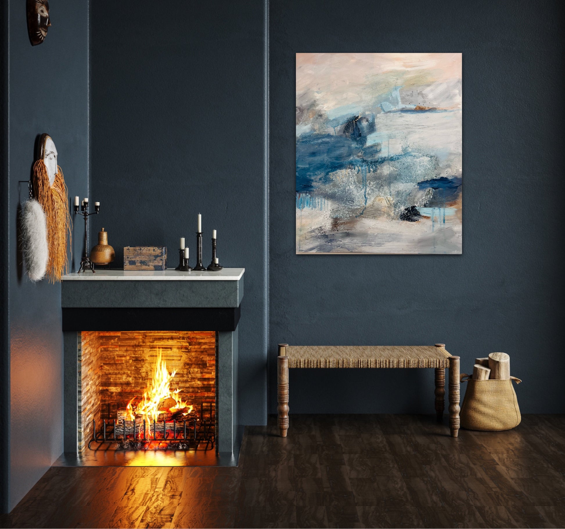 The atmospheric painting hangs on a dark blu wall above a rattan bench near to an open fire burning brightly