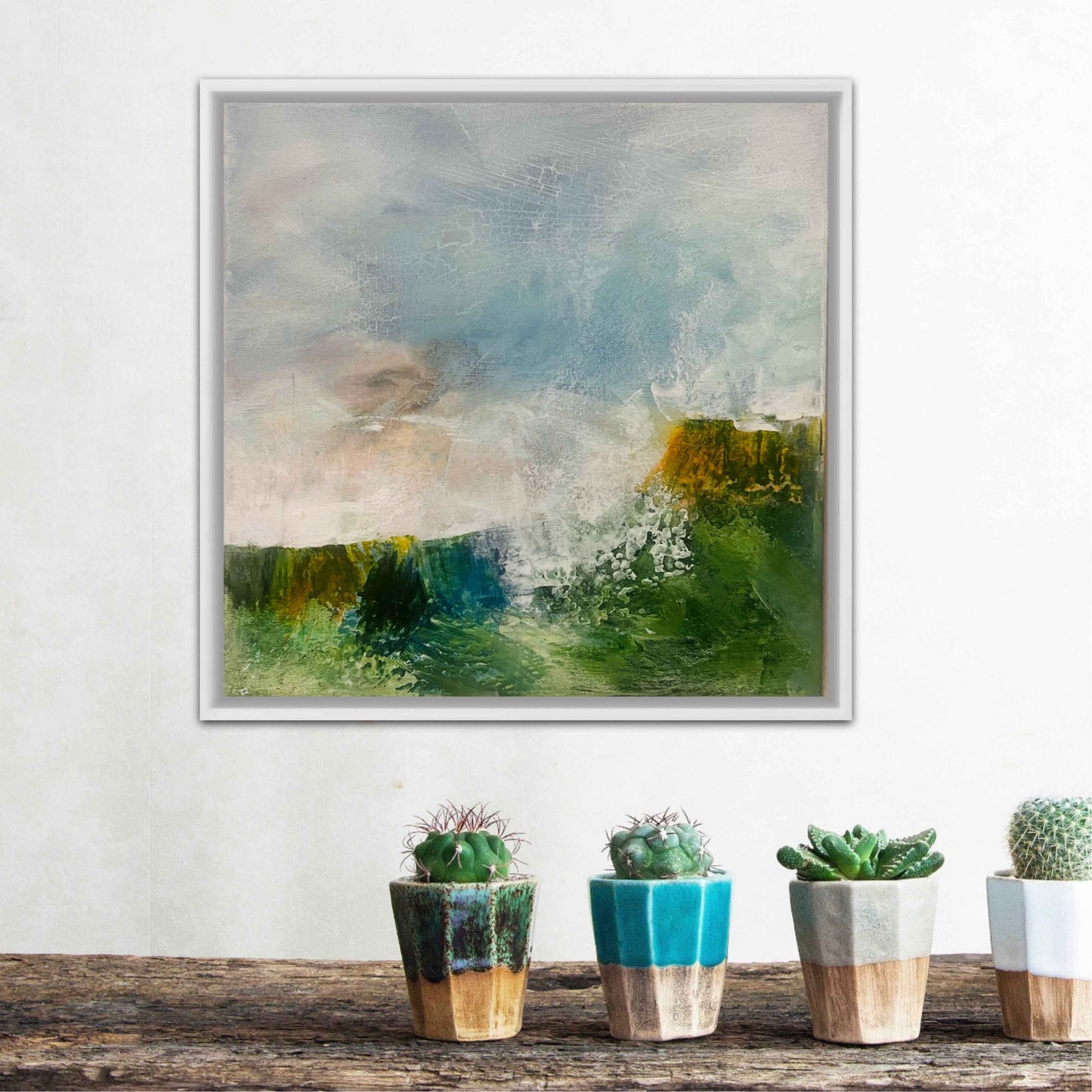 Framed abstract painting on a wall above a wooden surface with potted plants.
