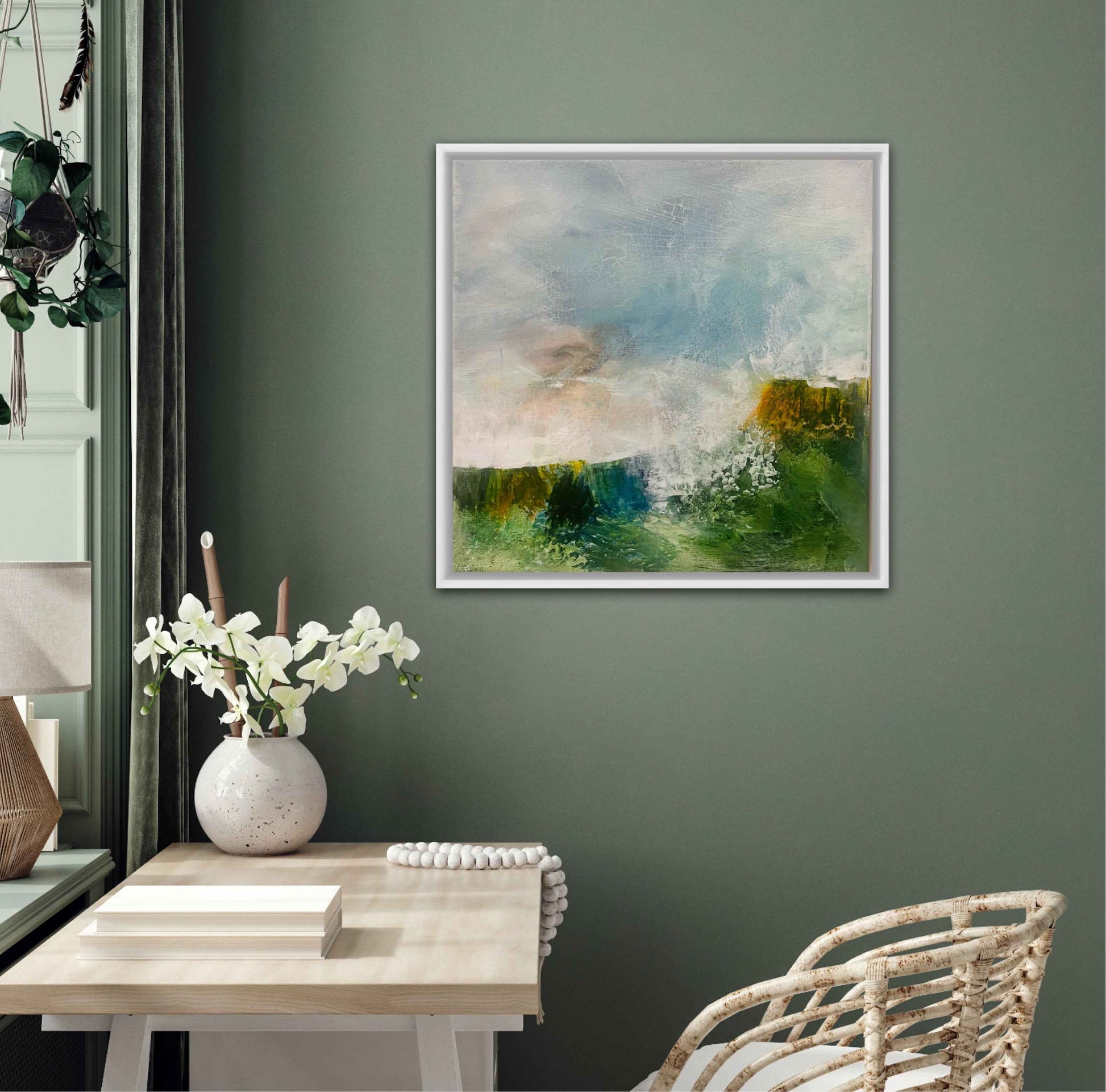 Framed abstract painting on a wall above a table with a vase of flowers and books.