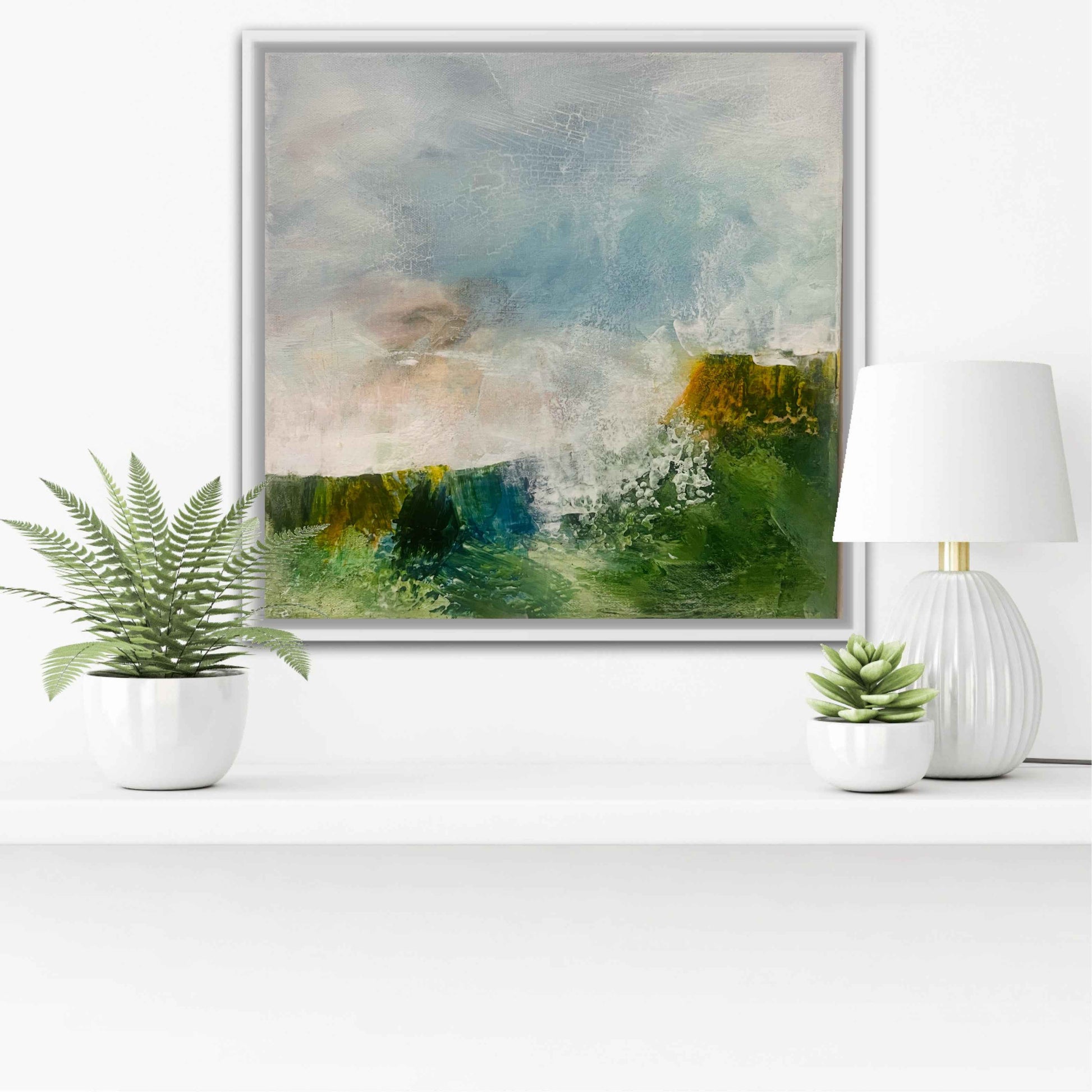 Framed abstract painting on a white wall with decorative plants and a lamp.