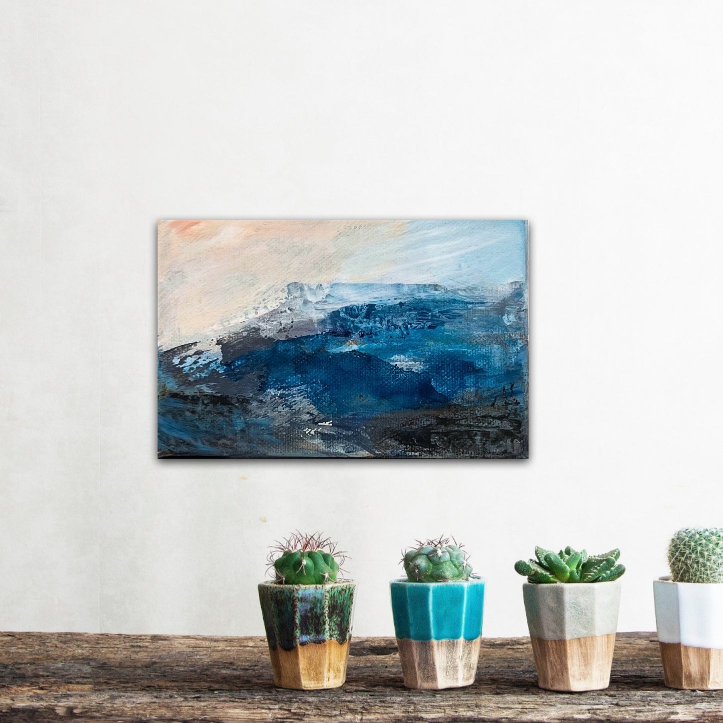 Fragments of Calm III original mini  blue and peach landscape painting on chunky box canvas  by contemporary British artist Nicola Briggsphoto on a wall with cactus plants in pots 