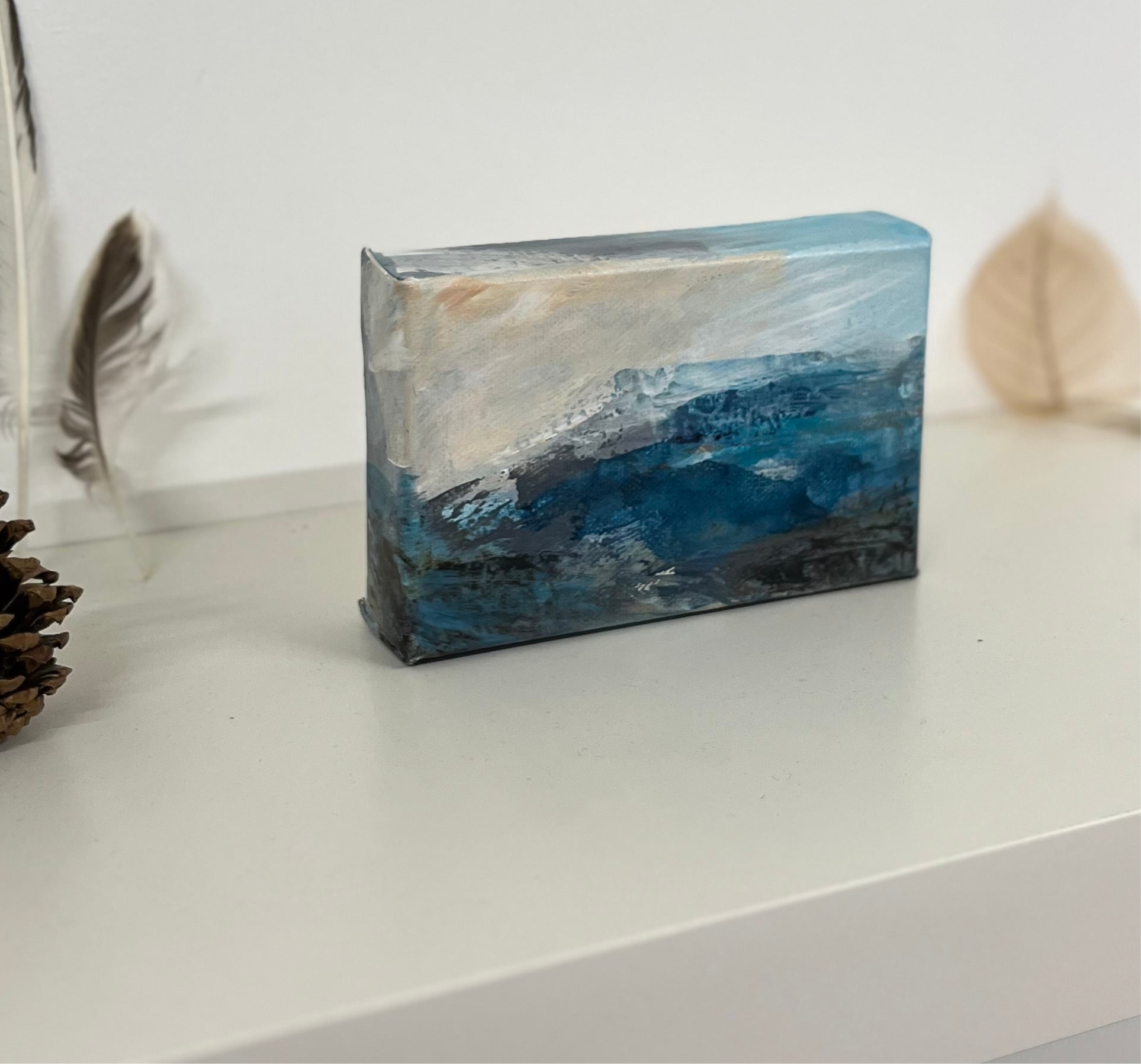 Fragments of Calm III small landscape painting by British contemporary Landscape artist Nicola Briggs photo shows box canvas near leaf for size