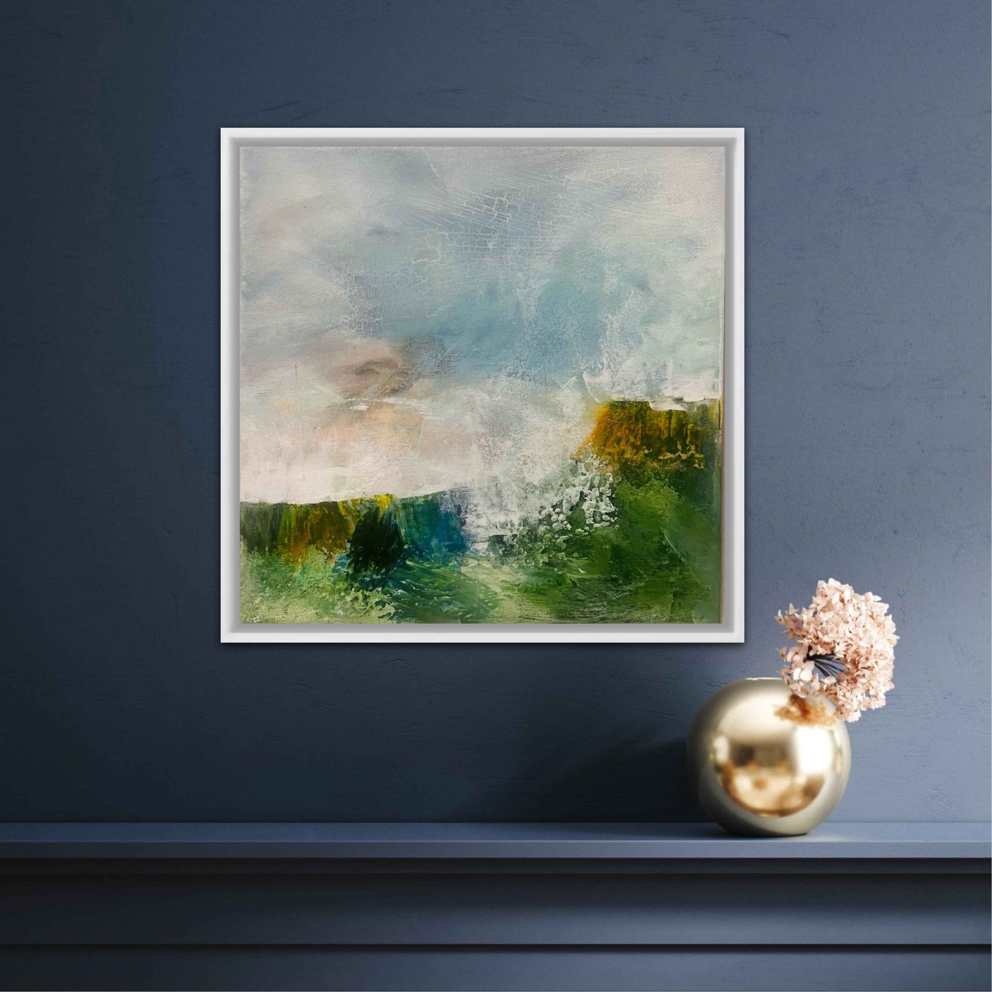 Framed abstract painting on a dark blue wall with a gold vase and decorative object below.