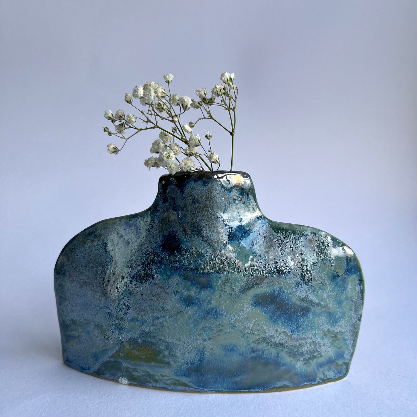 Blue ceramic vase with a textured surface holding small white flowers on a light gray background