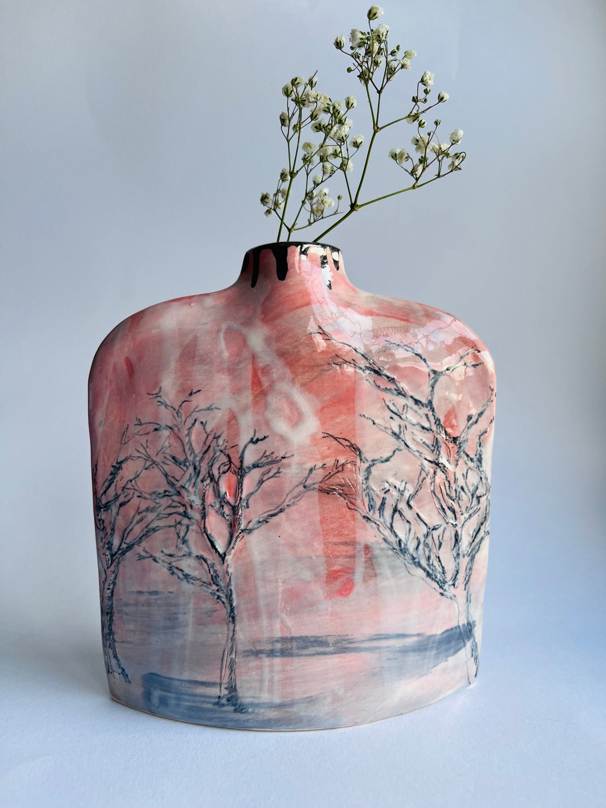 Ceramic vase with artistic tree design and a branch with small flowers on a light gray background