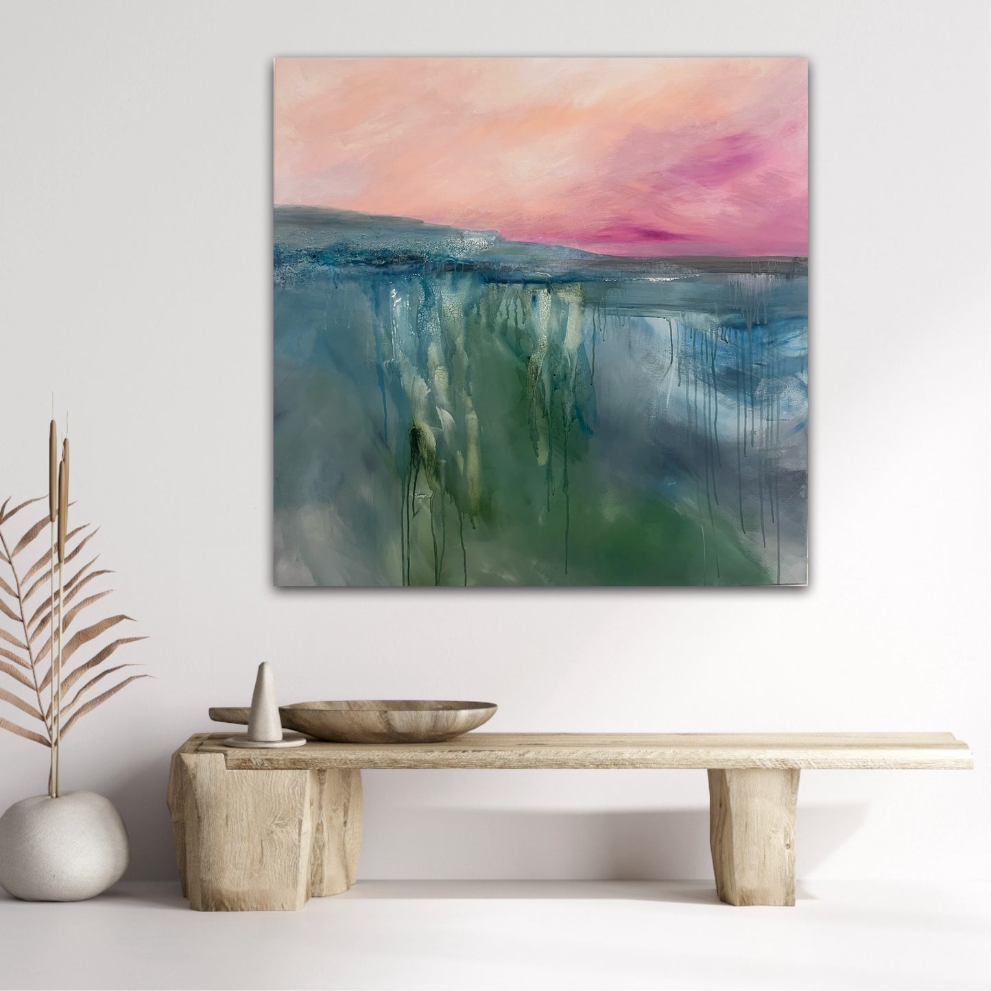 Abstract painting with colorful sky and water on a white wall above a wooden bench.