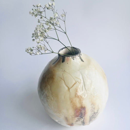 Decorative vorganic shaped oval porcelain ase with a natural finish holding small white flowers on a light background