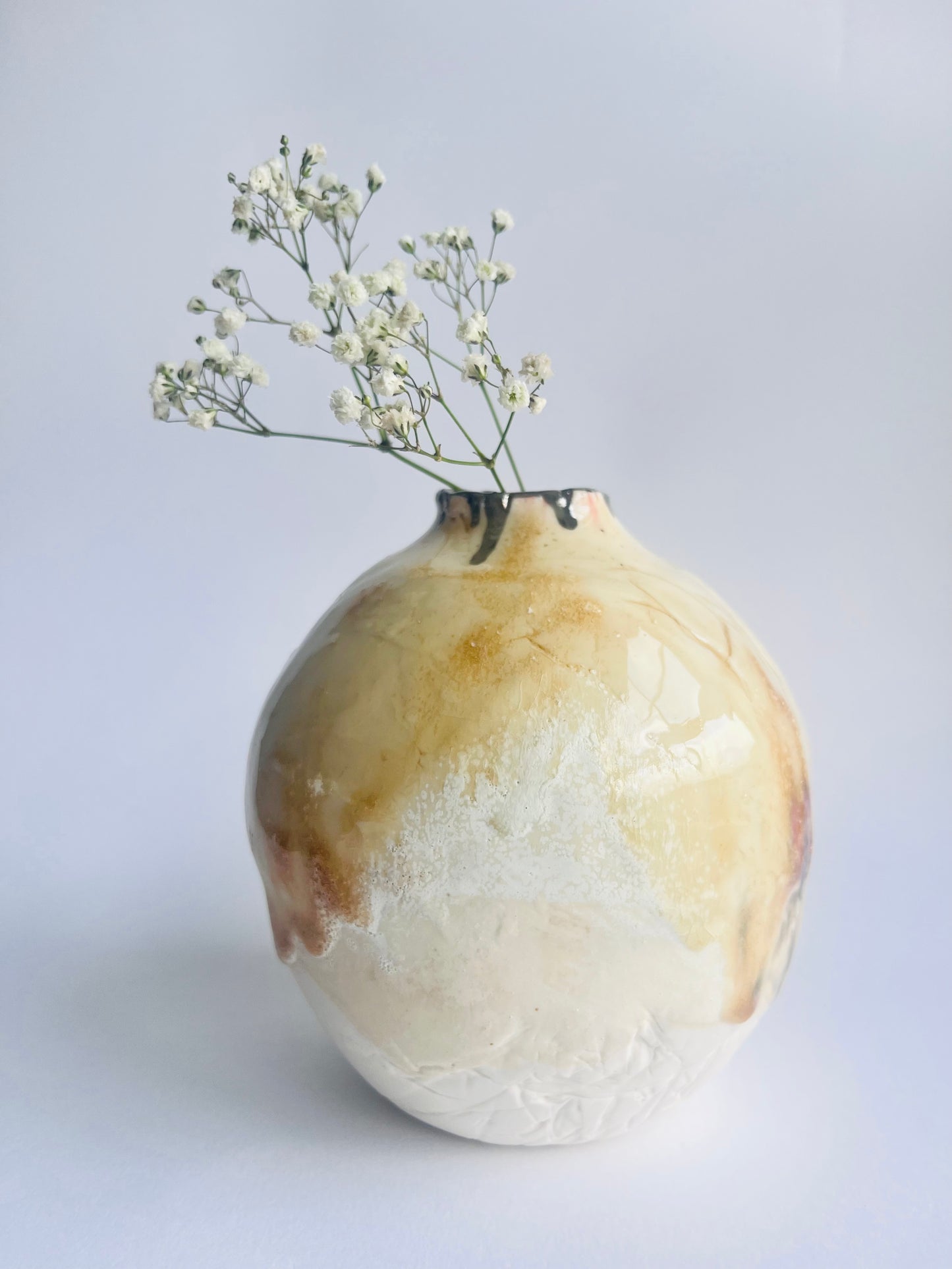 Organic shaped oval Vase with a natural, earthy finish holding small white flowers on a light background by Nicola Briggs 