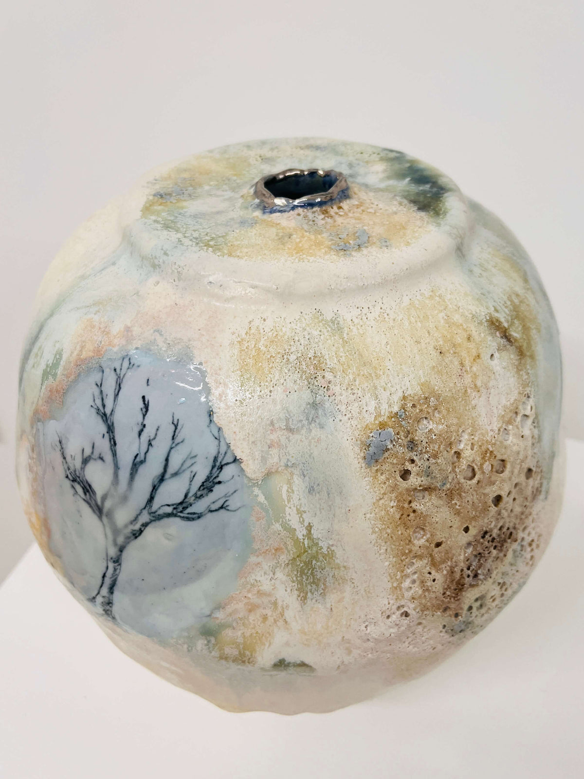 A handmade ceramic vase with a textured, porous surface and a painted tree design, displayed on a white surface against a white background.