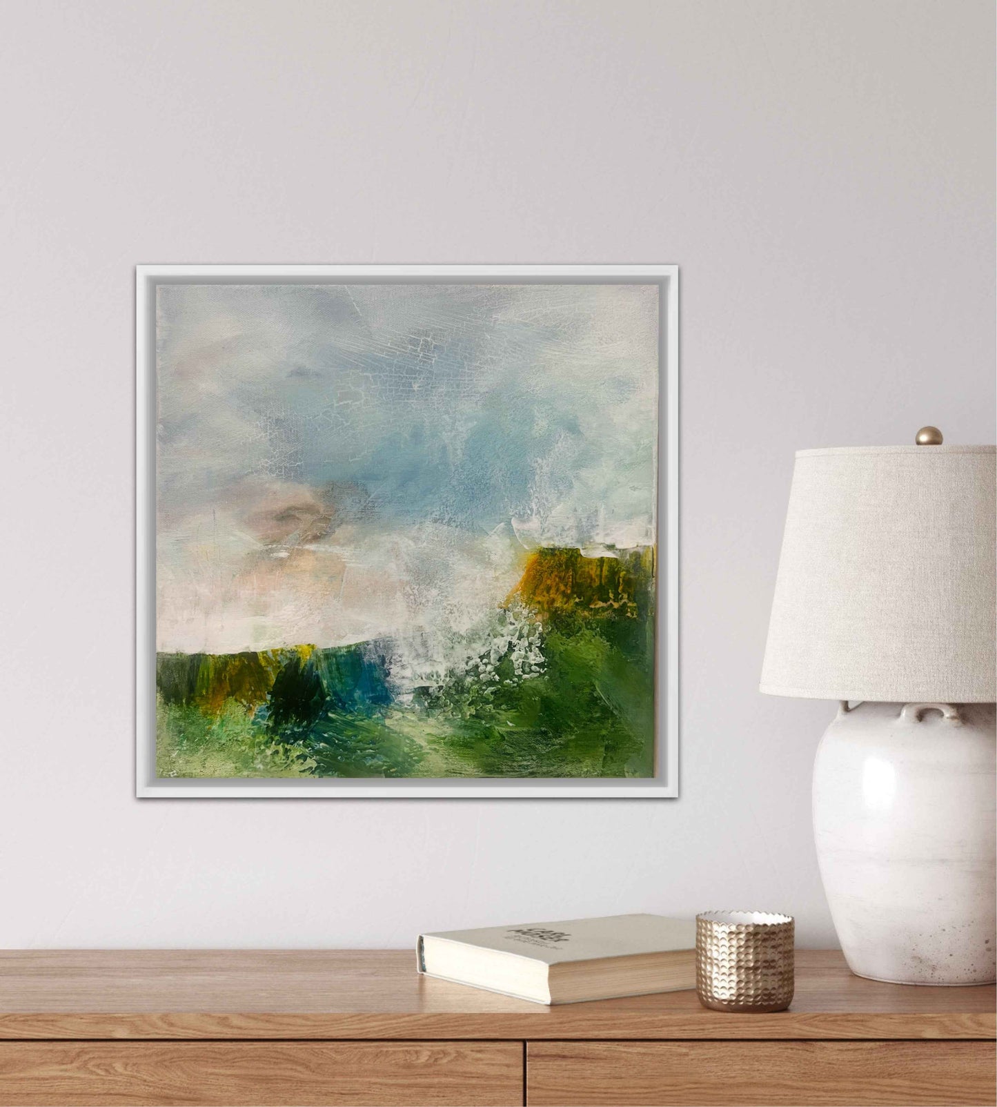 Framed abstract painting on a wall above a wooden console table with a lamp and books.